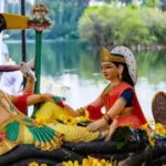 A vibrant idol of Lord Vishnu resting on Sheshnag with Goddess Lakshmi by his side, adorned with flowers, placed near a serene lake.