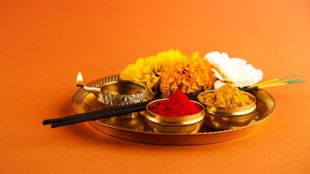 Traditional Hindu puja thali with marigold flowers, diya, incense sticks, kumkum, and turmeric on a brass plate for Indian festival rituals